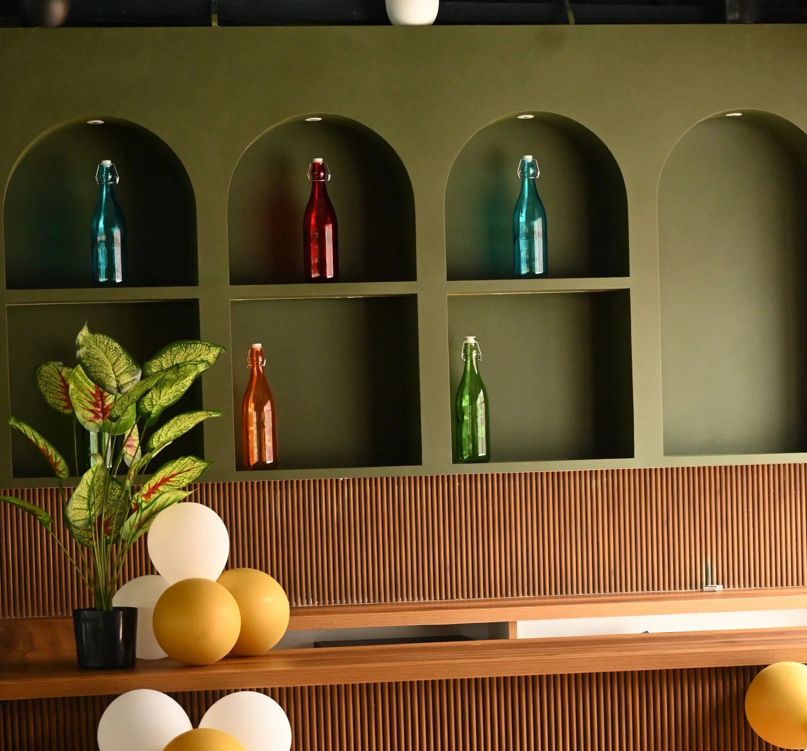 Café counter with colourful bottles in arched shelves, a plant and balloons