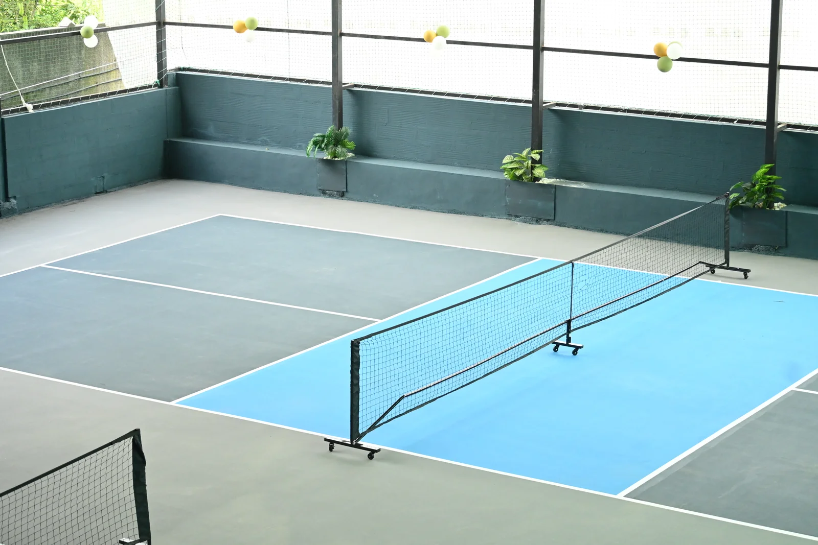 Indoor pickleball court with a blue kitchen area and net at Pickle & Cue Club